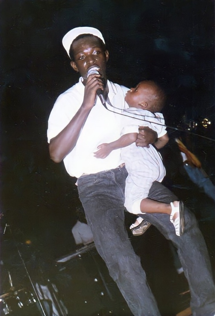Hamed Farras singing on stage, holding a microphone and a small child