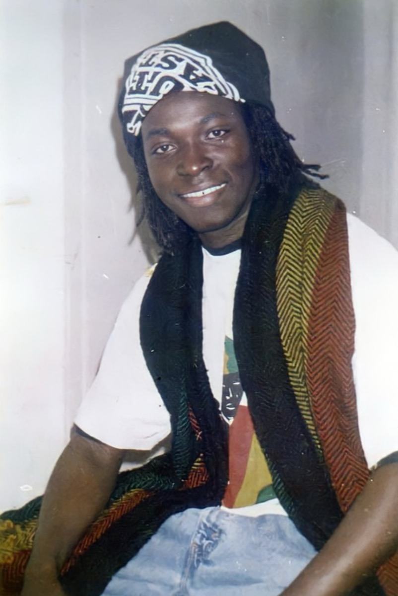 Hamed Farras smiling, with long locks, a patterned cap and a striped scarf